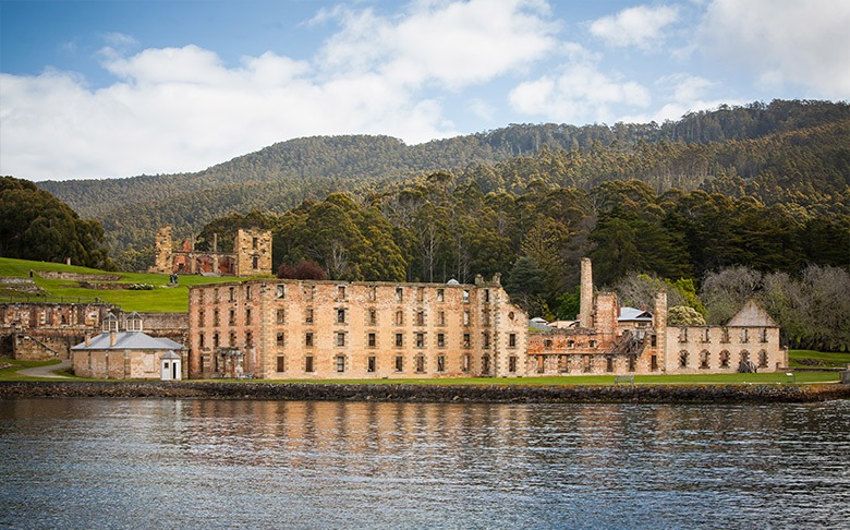 Port Arthur Historic Site on the Tasman Peninsula, featuring sandstone convict-era buildings along the waterfront with forested hills behind.