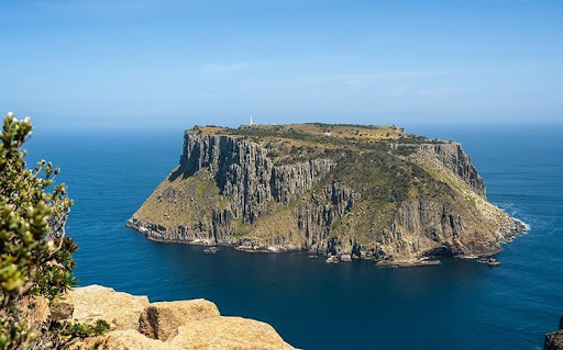Tasman Island off the Tasman Peninsula, with dramatic sea cliffs and the Tasman Island Lighthouse rising above the deep blue ocean.