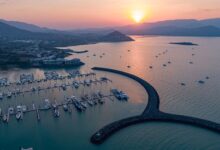 Airlie Beach marina in the Whitsundays at sunset, with boats anchored against a backdrop of coastal mountains.