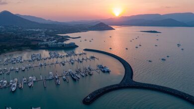 Airlie Beach marina in the Whitsundays at sunset, with boats anchored against a backdrop of coastal mountains.
