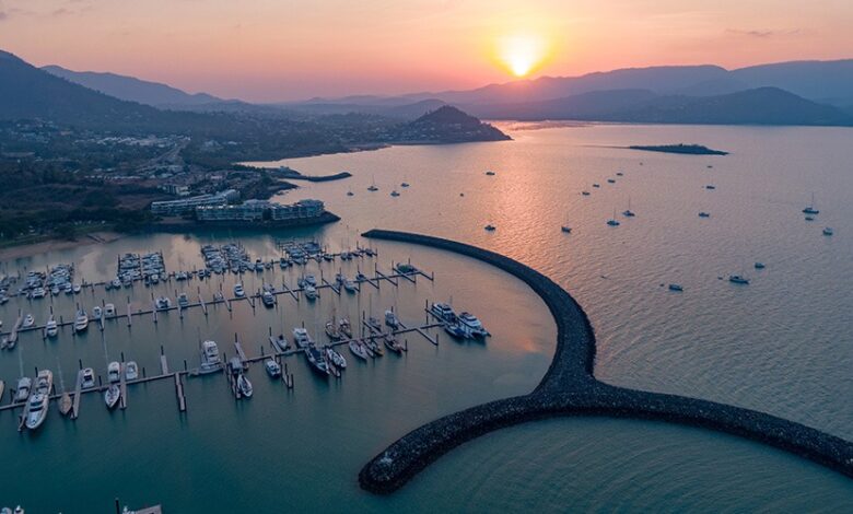 Airlie Beach marina in the Whitsundays at sunset, with boats anchored against a backdrop of coastal mountains.